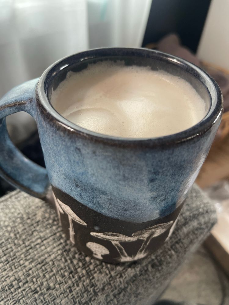 A chai tea latte in a blue and black mug with mushrooms on it. 