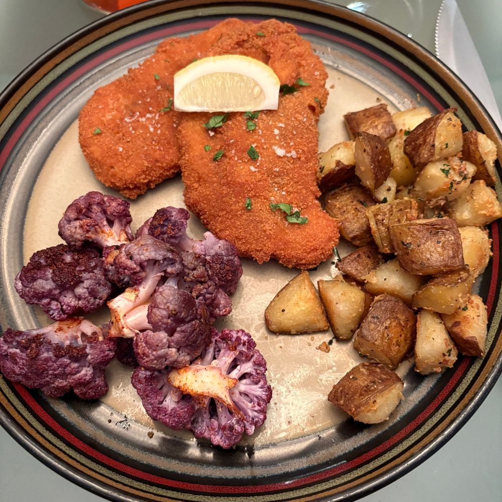 2 golden fried pork schnitzel cutlets, roasted potatoes and roasted purple cauliflower 