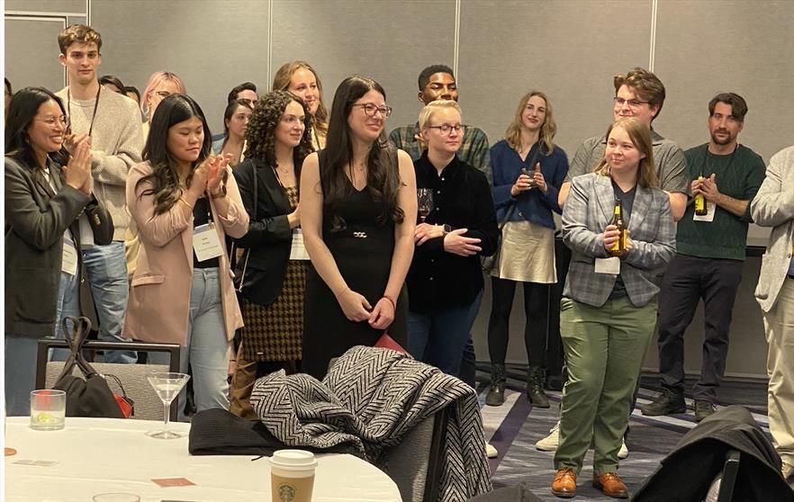 A group of people stand around listening to someone off camera.