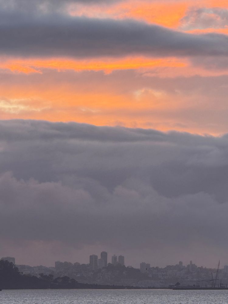 Orange, gold, gray sunset over San Francisco. Bay is gray. Slight haze of fog over the city.