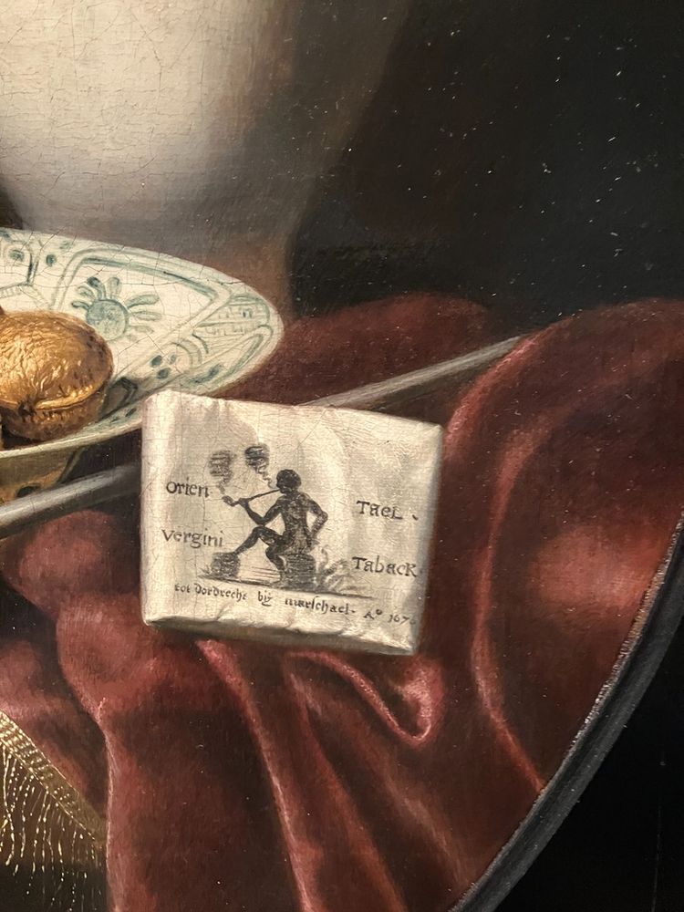 Cut-out of the paper tobacco wrapper, showing a Black man smoking a long-stemmed pipe and the text 'orien Tael / vergini Taback / tot Dordrecht by marschael / A 1670'