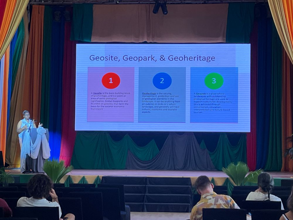 Photograph of Sherene James-Williamson at a podium talking in front of a slide titled geosite, geopark and geoheritage.