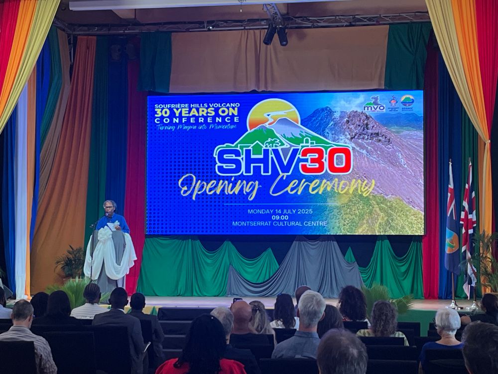Photograph of Dr Graham Ryan, director of the Montserrat Volcano Observatory standing in front of the SHV30  banner at the opening ceremony of the Soufrière Hills 30 years on conference, Montserrat 