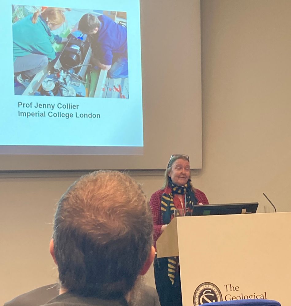 Photograph of Prof Jenny Collier, Imperial College, accepting the Murchison Medal, in front of an image of Jenny inspecting an instrument on board a research ship