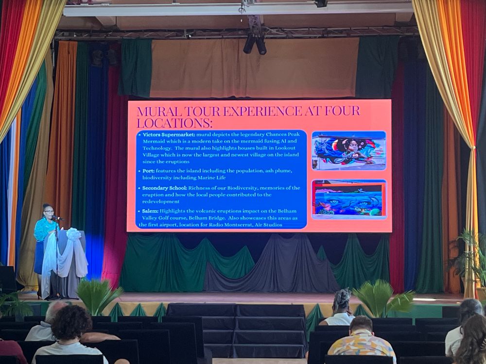 Rosetta West Gerald speaking at a podium in front of a slide on the Montserrat Murals tour 