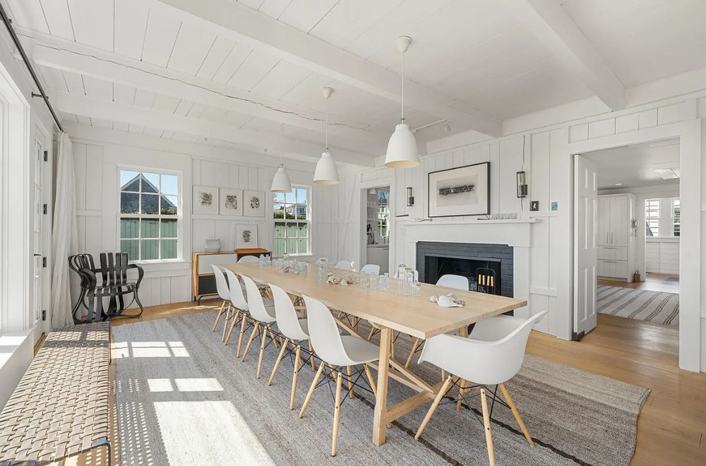 a dining room styled in white and agreeable gray. the dining chairs are white plastic seats with light wood legs that bow out, held together by black crisscrossed rods. you could call it casual minimalism