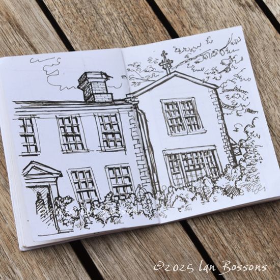 An open sketchbook showing a black fineliner drawing of the corner of a large house, with its open doorway on the bottom left. There are lots of bushes in front, with tree branches on the right and a cloud behind.