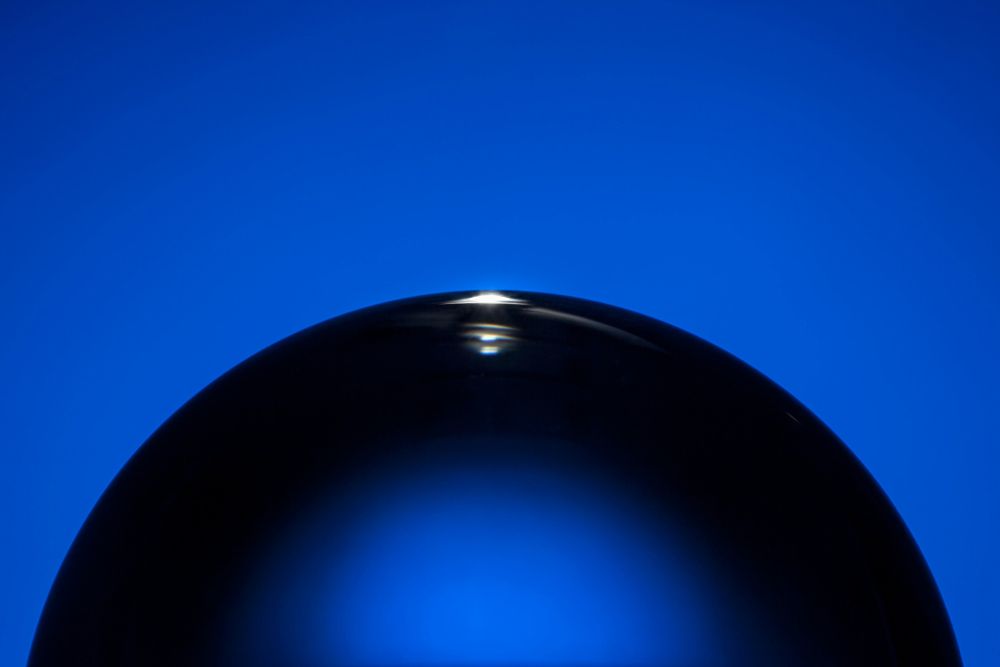 Close up of top half of an clear acrylic sphere on blue background.