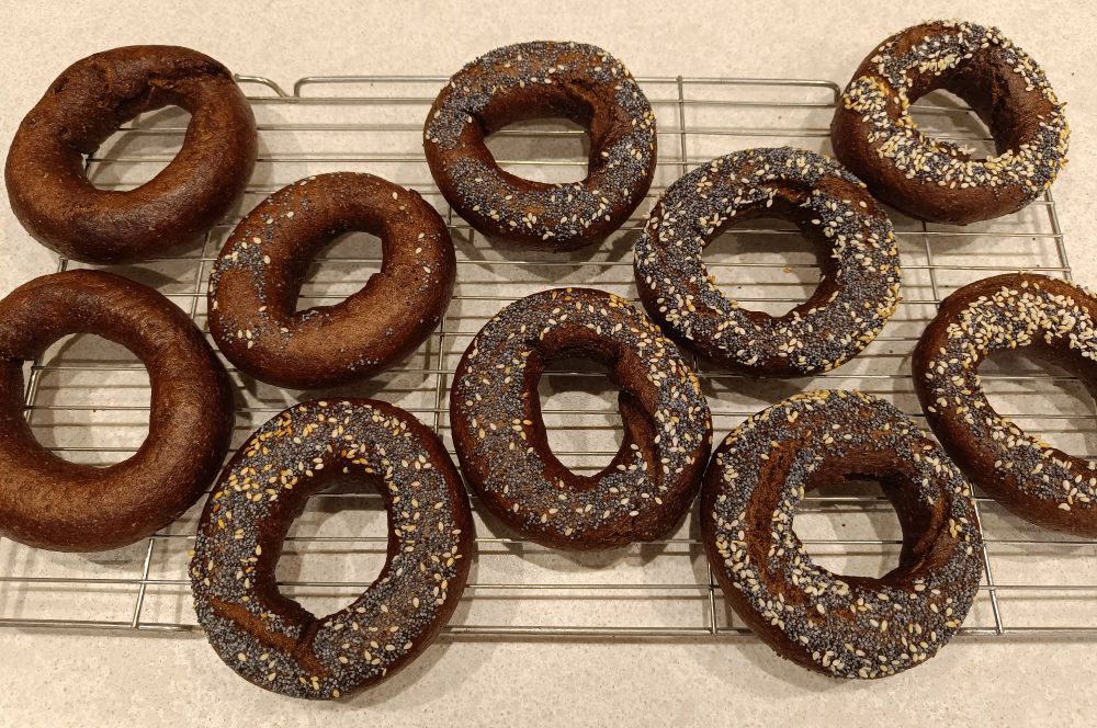 Cooling rack with ten homemade chocolate coloured bagels that look like dog turds