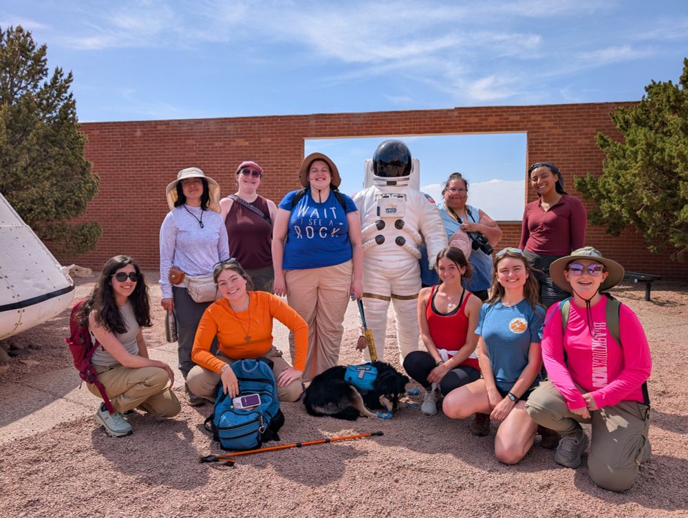 10 students gathered around a life-sized statue of an astronaut in a courtyard with desert a vista in the background 