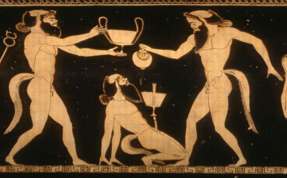 image from an athenian pot, red figures on a black background, showing a group of satyrs playing drinking games. One is leaning back carefully resting a chalice on his phallus, while another pours wine into it