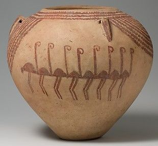 a simple ceramic jar with a light red on tan decoration. In the center is a row of birds drawn in a simple, stylized fashion. They have long legs and a long neck ending in a curly-q shaped head. The color and shape gives them a strong resemblance to a line of flamingos doing their famous dance shown frequently in nature documentaries often voiced by David Attenborough