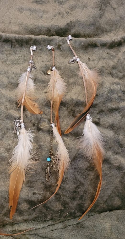 Drei Dreadperlen mit jeweils 2 Hühnerfedern dran und kleinen blättern aus Metall und ein paar Kugeln. Alles an einem langen Lederband befestigt.