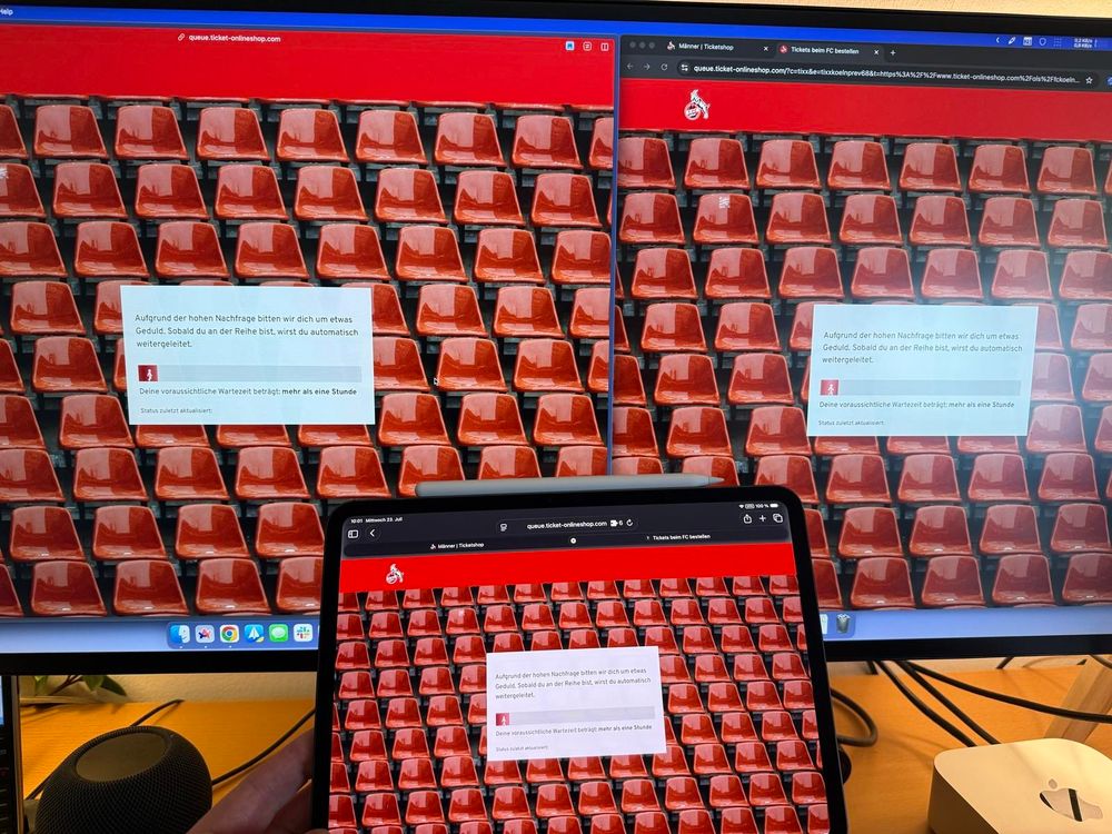 Mehrere Bildschirme und ein Tablet zeigen die Warteseite des FC-Ticketshops mit dem Hinweis auf hohe Nachfrage und eine Wartezeit von mehr als einer Stunde.