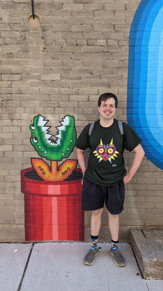 A picture of me standing next to a mural painting of a Piranha Plant while wearing a Majora's Mask shirt