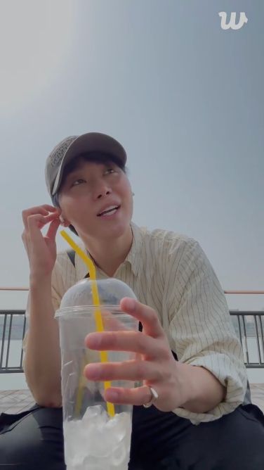 seungkwan squatting down and talking while holding a cup with ice and a straw in it