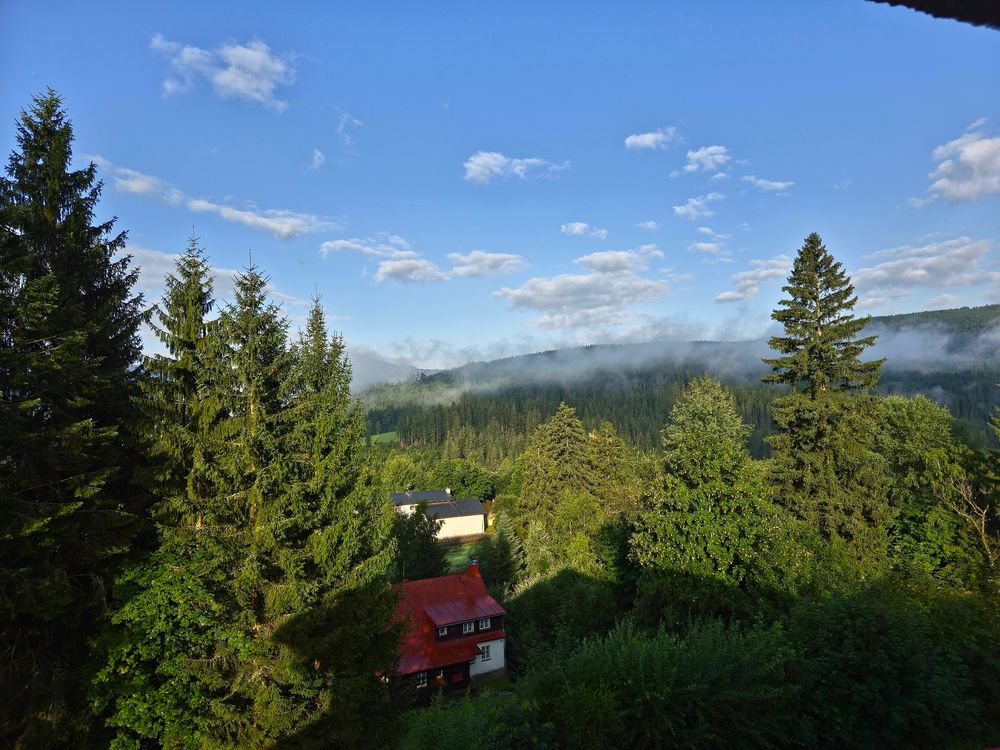A beautiful view of the mountains with a bit of morning mist and a small house in the foreground. 