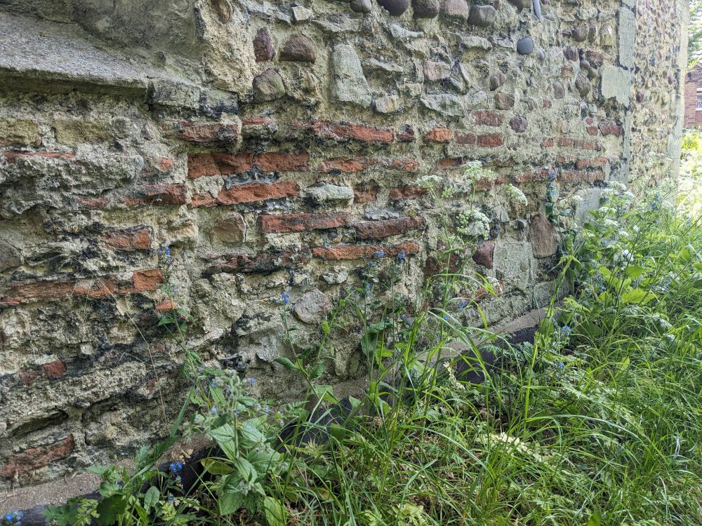 A close-up of the construction of the church nave wall showing narrow flat red brick tiles amongst the stonework.