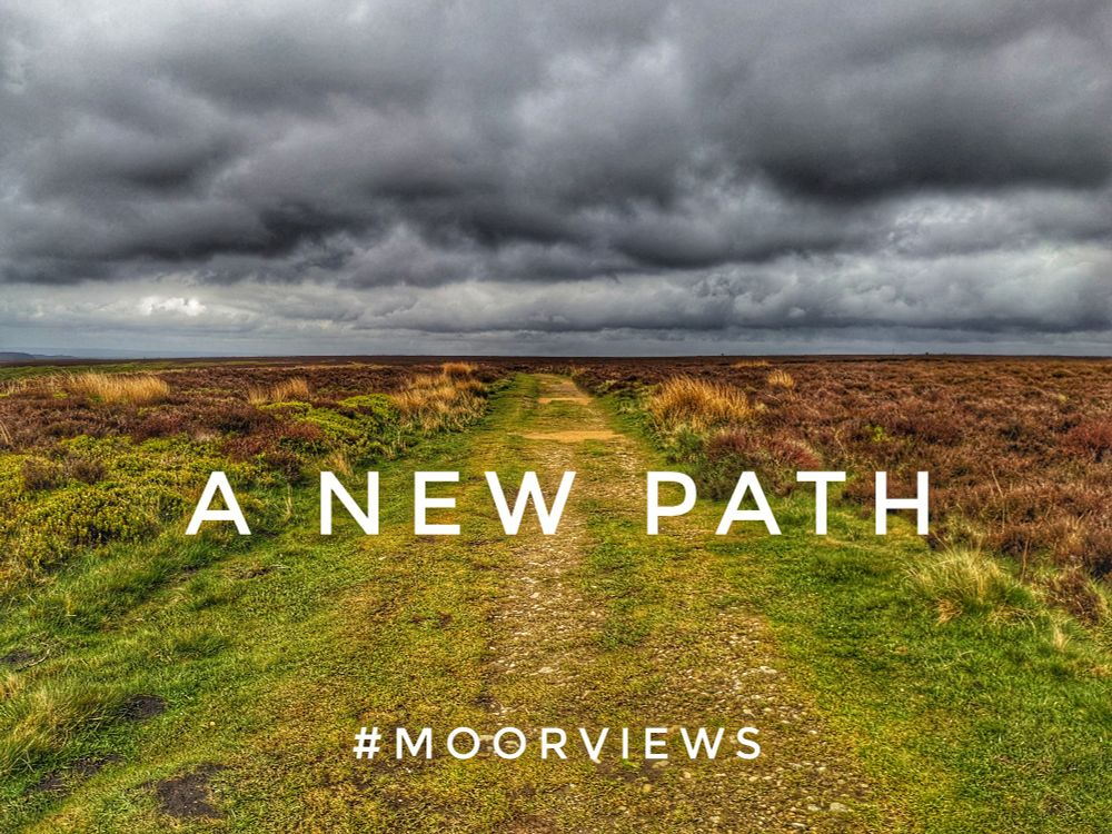A footpath across a flat moor landscape with a grey cloudy sky. The text reads 'A new path #moorviews'