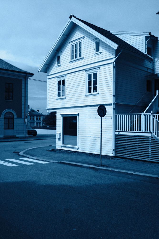 A landscape photograph featuring the Norske Soltak building - which is adjacent to Vår Frelsers kirke in Haugesund, Norway - standing on a desolate street on a mostly cloudy afternoon.
