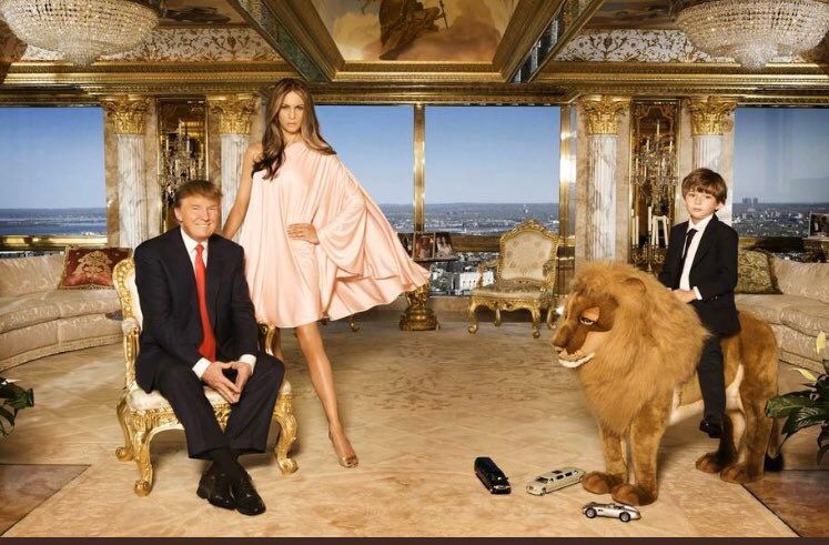 Donald, Melania and a young Barron Trump posing in their gilded apartment overlooking New York City. Barron is sitting on a tall plush male lion, with toy cars at its feet, two of which are limousines. Every possible surface of the room is covered in cheap looking gold. Donald has a wide smile but his wife and son look miserable, as always.