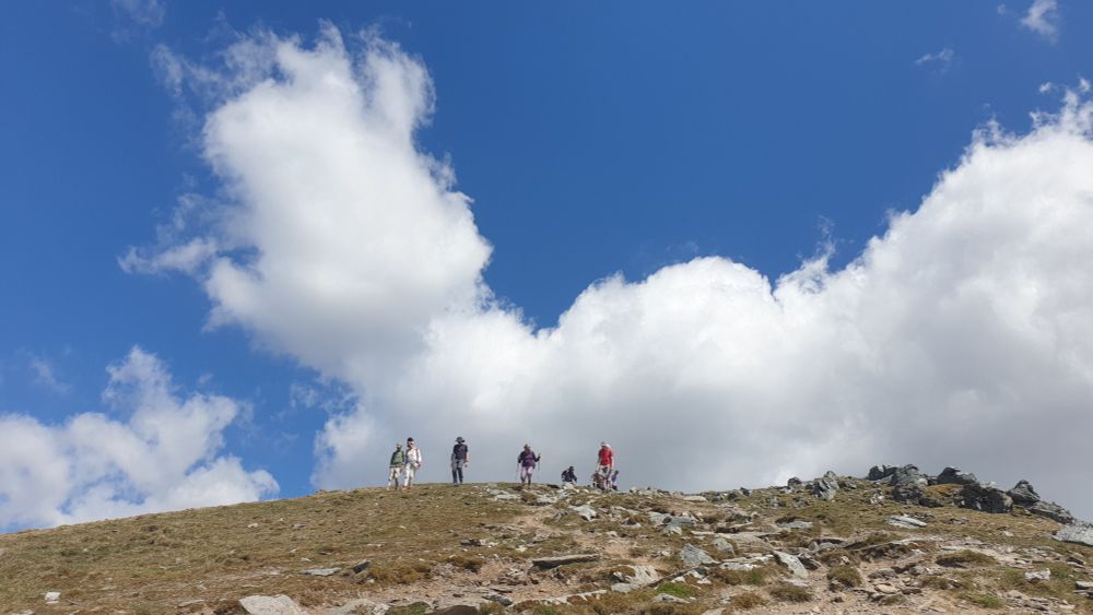 People walking down a rocky mountain side with a blue sky and a big white cloud behind them.