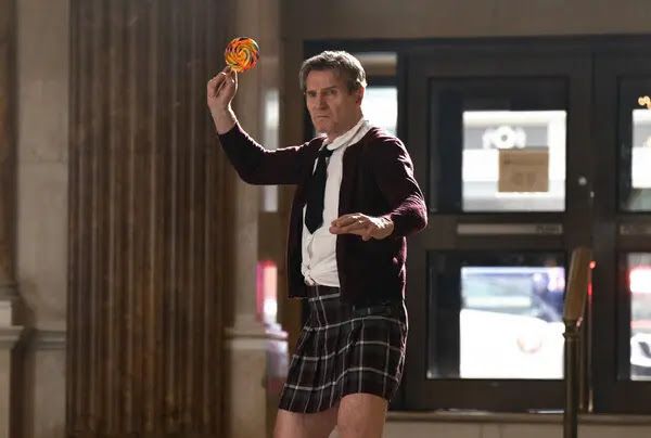 Lt. Frank Drebin Jr. (Liam Neeson), dressed in a schoolgirl's uniform, threatens to throw a multicoloured lollipop at an offscreen opponent in a still from Akiva Schaffer's THE NAKED GUN.