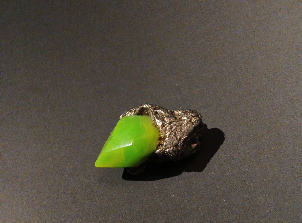 a physical model of a zat-zhing TF trigger from Out-of-Placers, consisting of a faux-crystal made of cast UV reactive resin and a polished Campo Del Cielo meteorite