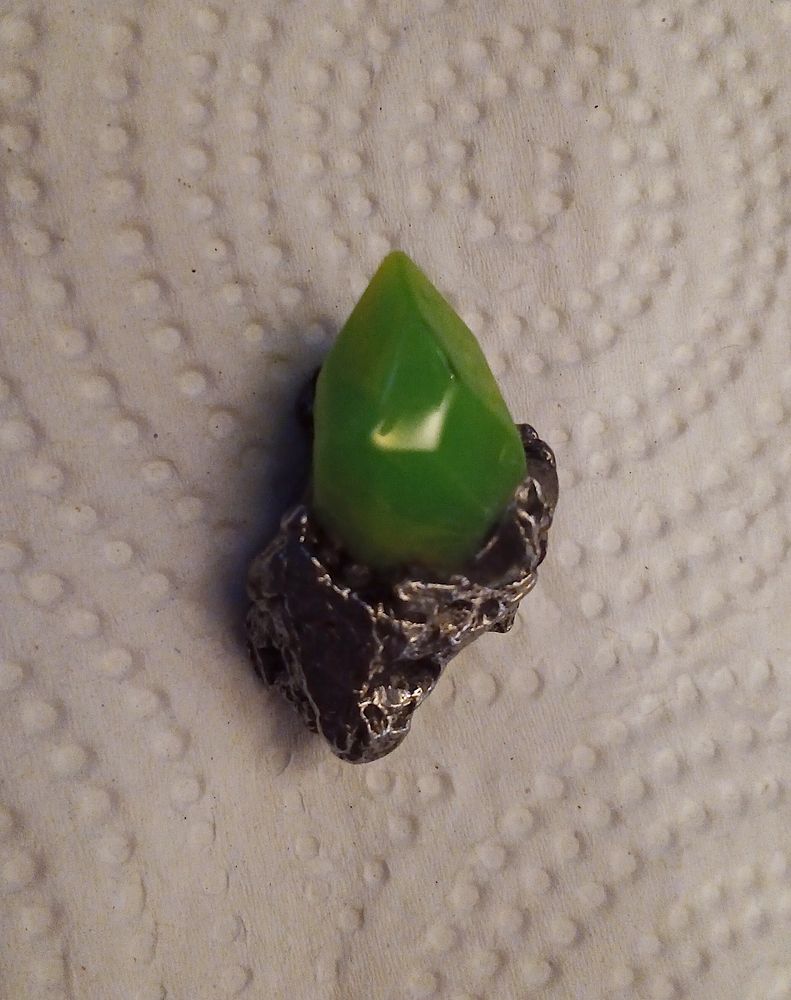 a physical model of a zat-zhing TF trigger from Out-of-Placers, consisting of a faux-crystal made of cast UV reactive resin and a polished Campo Del Cielo meteorite