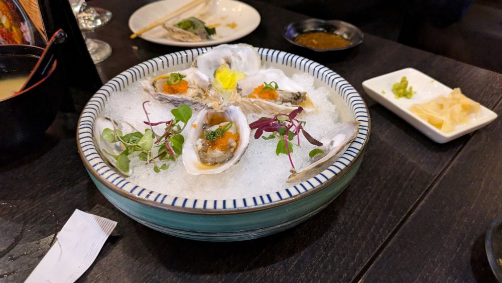 three oysters sitting in a round bowl surrounded by garnish on a black wooden table