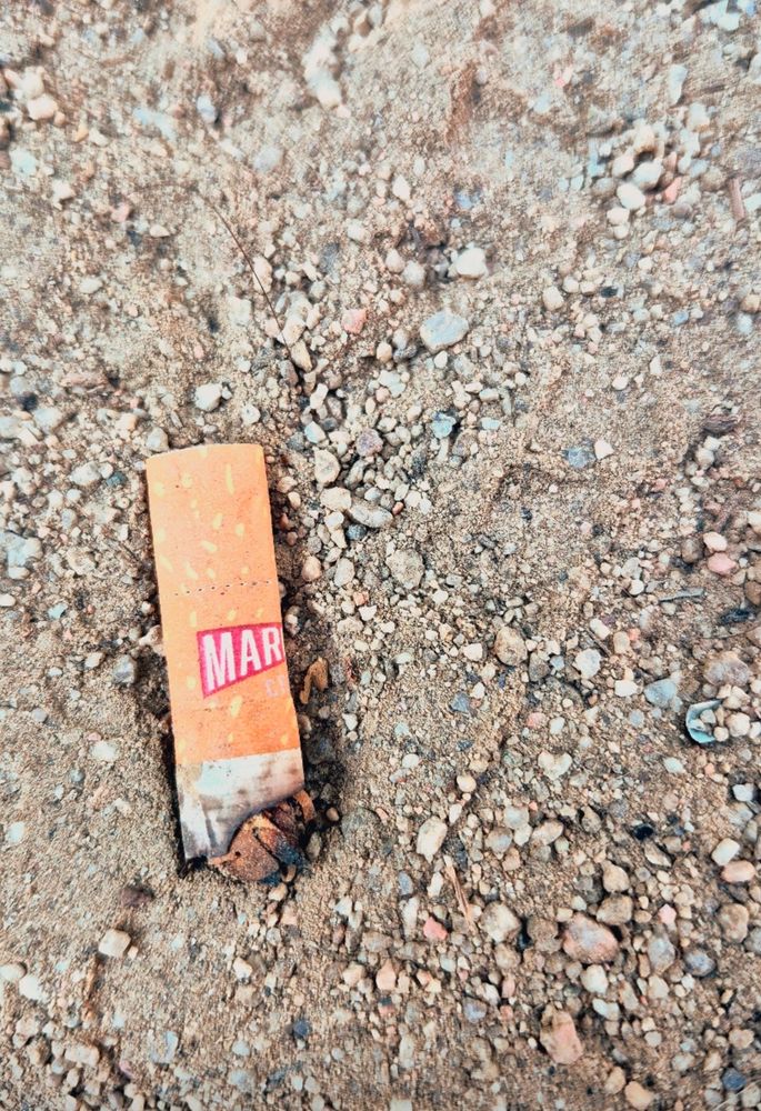 Zigarettenstummel liegt auf sandigem Boden. Auf dem Stummel ist rote Logo einer 'Marlboro' zu erkennen. Es sieht dem marvel Logo ähnlich.