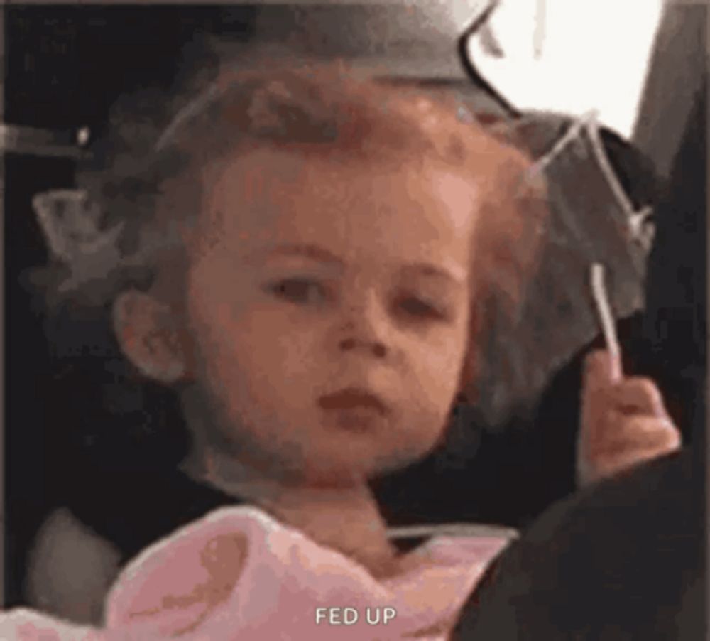 a little girl is sitting in a car seat holding a lollipop and making a funny face .