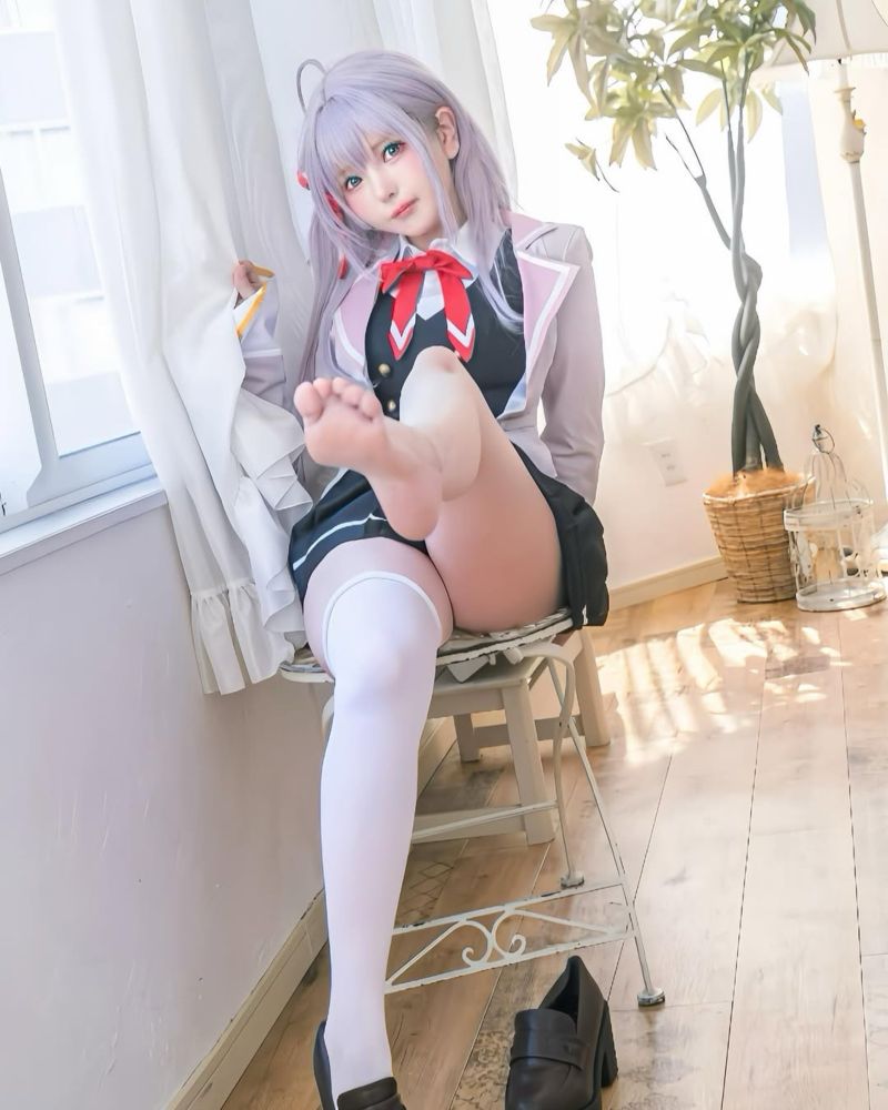 Girl on sitting on a chair wearing a school uniform with a mini-skirt. One of her two knee-highs is off, she lifts her bare leg towards the camera.