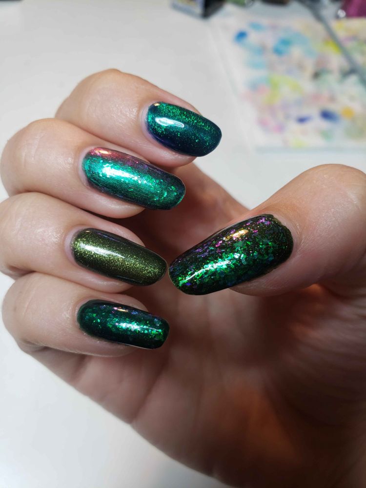 a hand with painted nails. Used, from pinky to thumb, an old dark green, Cirque Colors' Draco, Holo Taco's Missed Shift, Mooncat's Drown My Demons, and an old olive-green glitter. the dark green, missed shift, and the olive glitter got topped with Holo Taco's Galactic Unicorn Skin. Draco is a dark green magnetic, Drown my Demons is an indigo and green magnetic, and Missed Shift is a multichrome that goes from green to purple