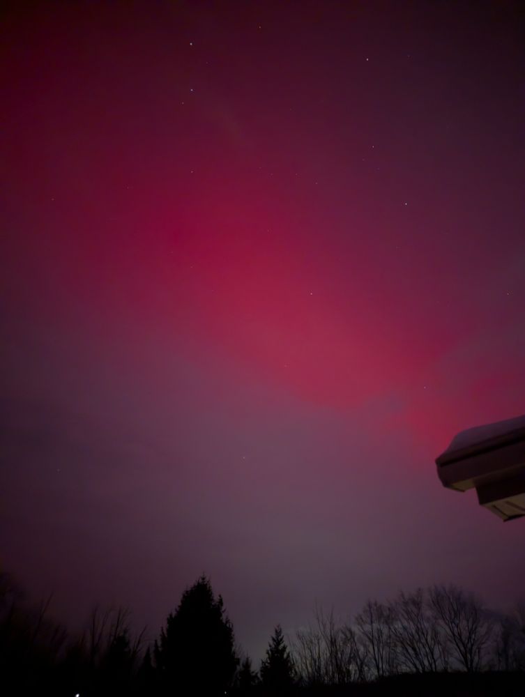 A night photo of the sky with a large pinkish red splash of color across it.
