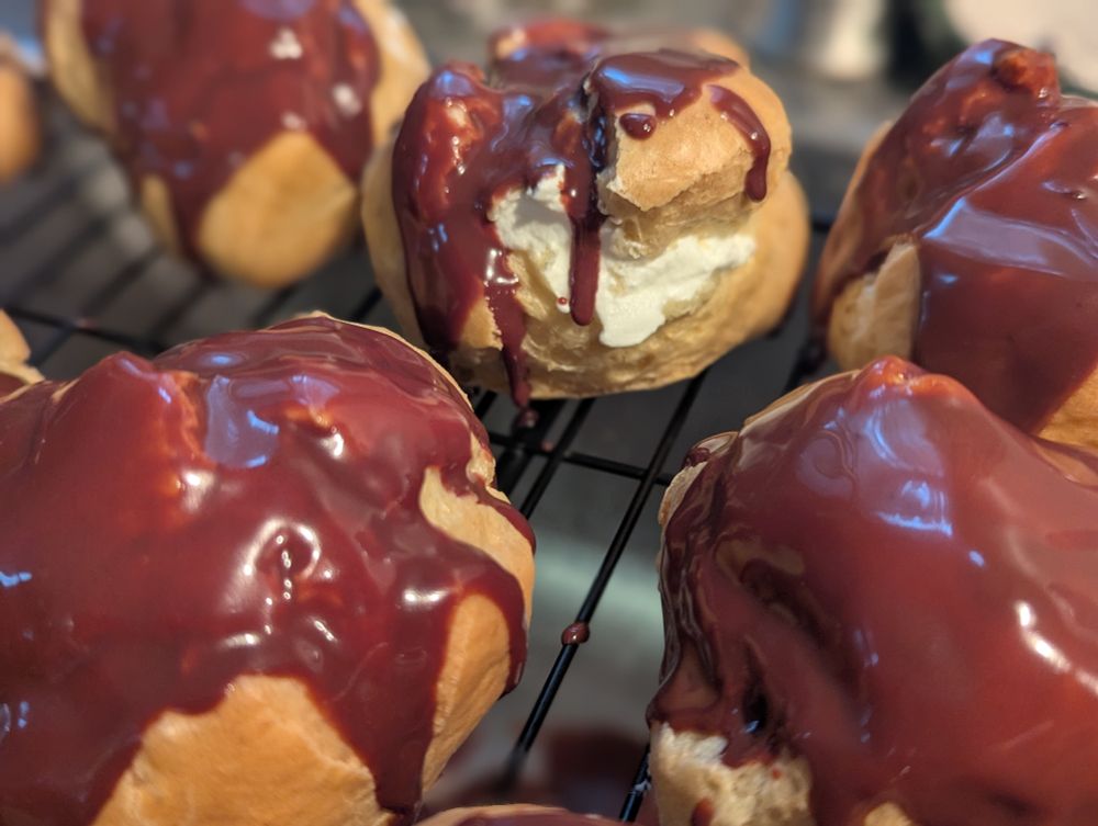 A close up photo of chocolate drizzled on creme profiteroles.