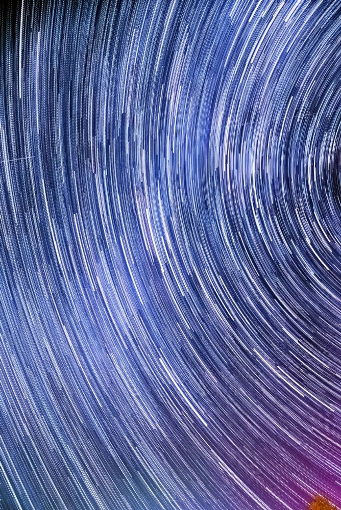 Image of Stars trailing around the north celestial pole with a slight amount of pinkish aurora appearing in the lower right corner