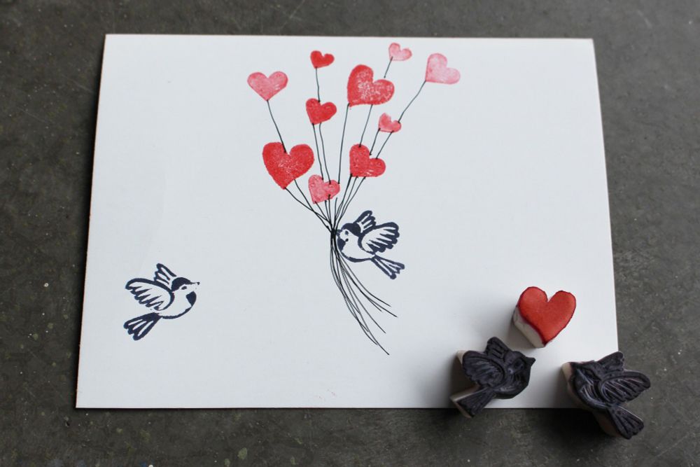 Handmade card with stamped birds and heart-shaped balloon designs. Rubber stamps of the birds and a heart are places on the bottom right of the card. 

