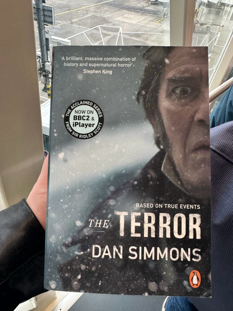 me holding a copy of Dan Simmons’ The Terror. Ciarán Hinds is pictured on the cover and looks suitably terrified 