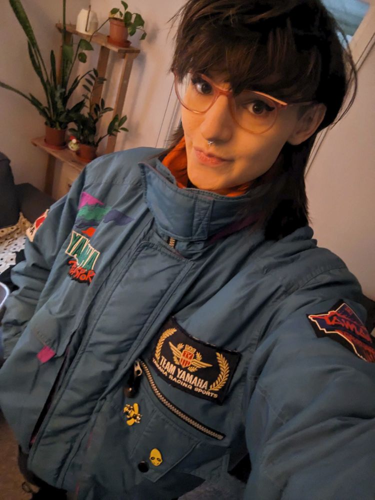 Picture of Samantha in a teal/cyan motorcycle racing jacket with varioys Yamaha patches.