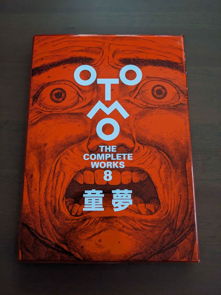 A picture of Domo, The Complete Works, a red bound manga volume with a detailed illustration of a man's horrified face on the front cover.