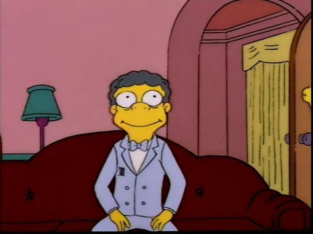 Screenshot of Moe from the Simpsons in a fancy suit, sitting on a sofa while smiling and looking very goofy.