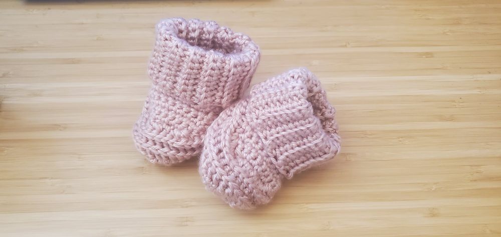 A pair of crocheted baby booties on a wooden desk