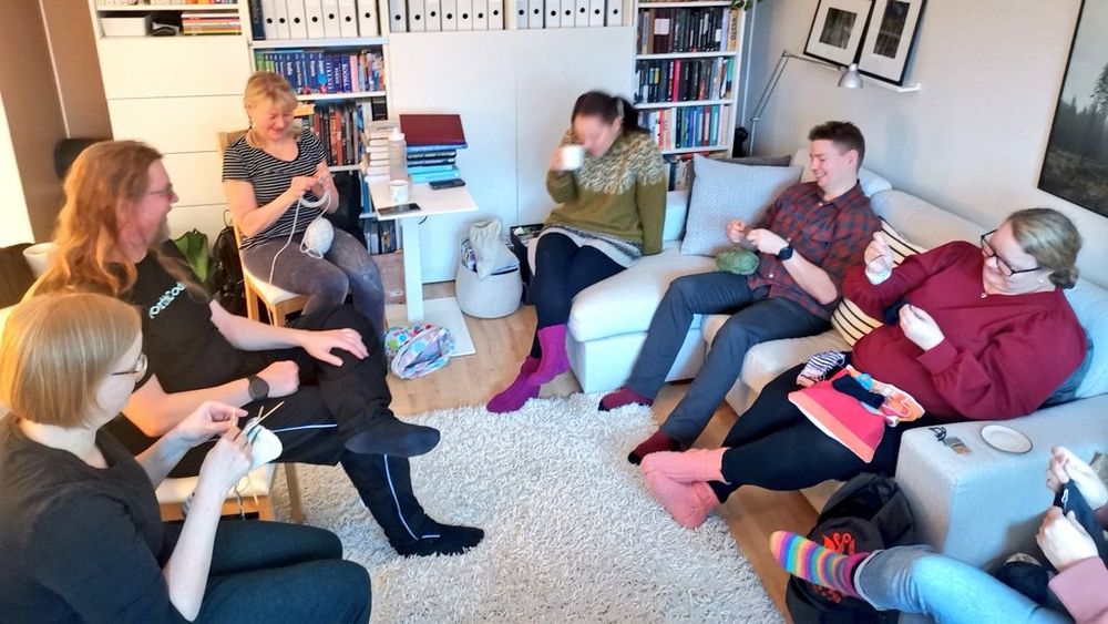 Iloisia ihmisiä istumassa neulomassa ja glögiä juomassa.