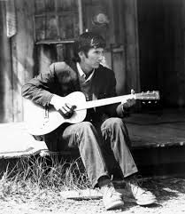 Middle age white male sitting on a wooden porch holding a guitar 