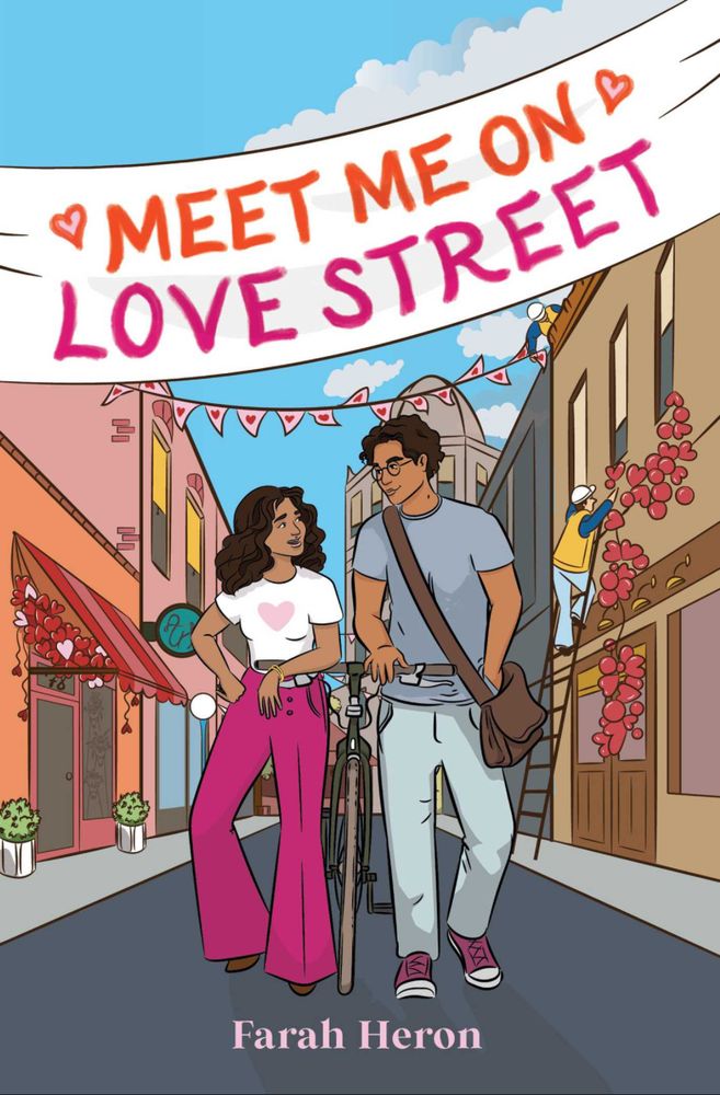 Cover image for Meet me in love street. In cartoon style the artwork shows a boy and girl walking down a street with a bike in between them. They are looking at each other. The girl has long curly brown hair and is wearing a white Tshirt with a pink heart on it and bright pink pants. He boy has short brown hair  and is wearing a grey Tshirt and pants. The street they are walking down has two story buildings on one side there is an awning with hearts dangling from the side. The other side of the street someone is on a ladder putting up a line of heart balloons. A banner of hears stretched across the street behind the couple. 