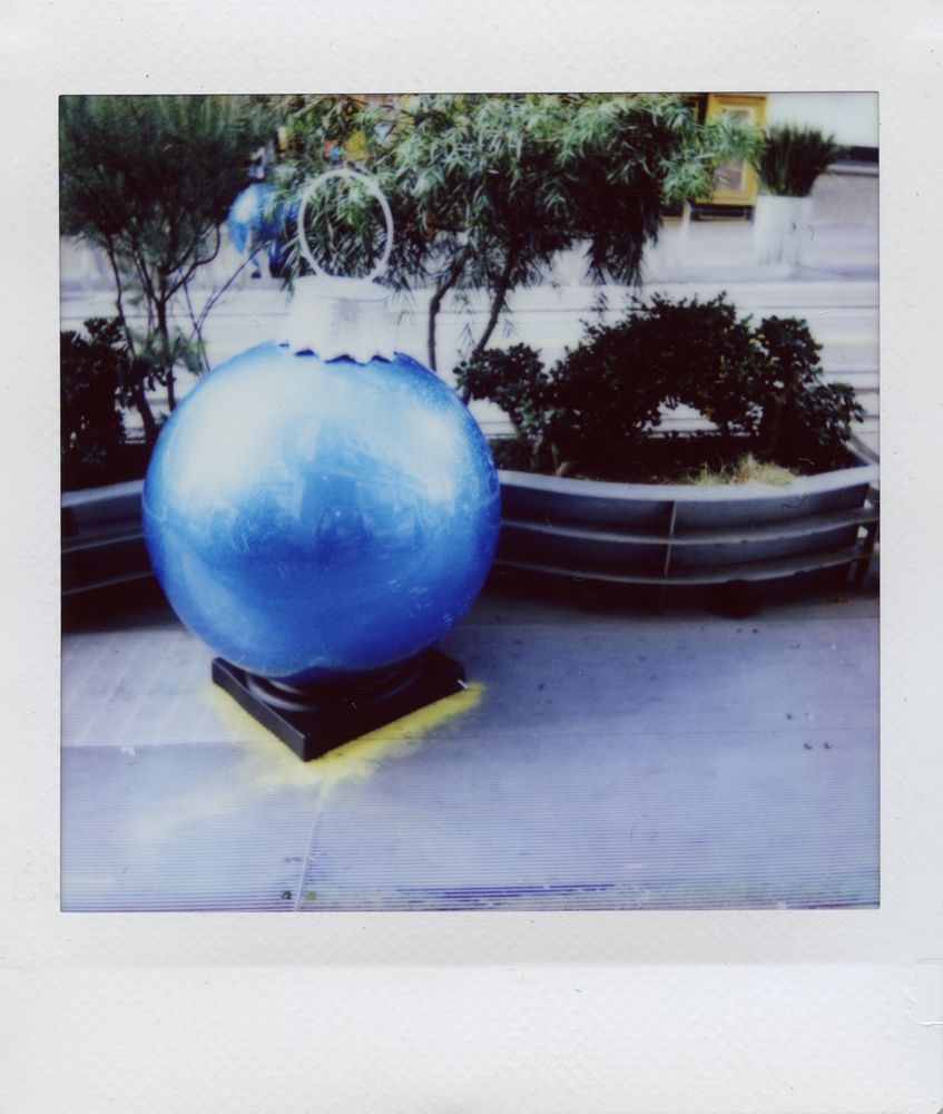 A sculpture in the shape of a giant blue sparkly christmas ornament sits on the sidewalk in front of an undulating planter