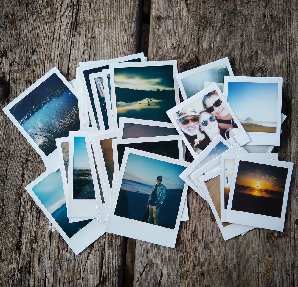 A pile of Polaroid pictures are spread out on a picnic table.
