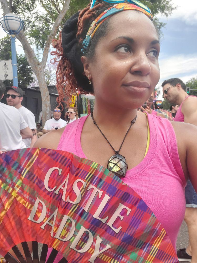 Markeia is holding a caftan print fan that says "Castle Daddy"