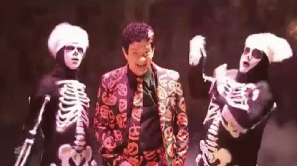 a man in a suit and tie is dancing with two skeletons .